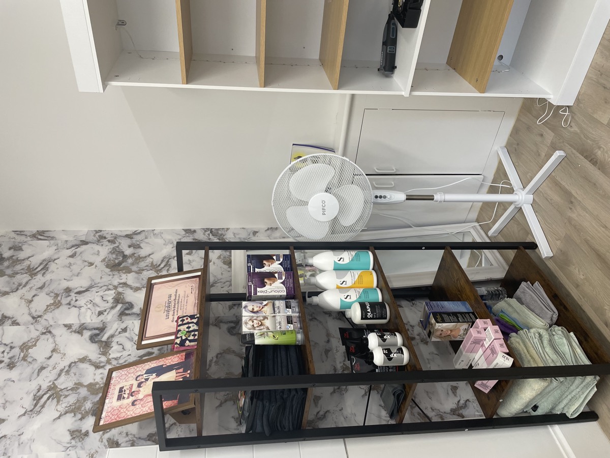 Shelving with salon products, folded towels and framed certificates