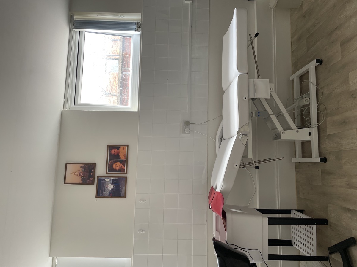The treatment room with a reclining facial bed, white tiling and family photographs on the wall
