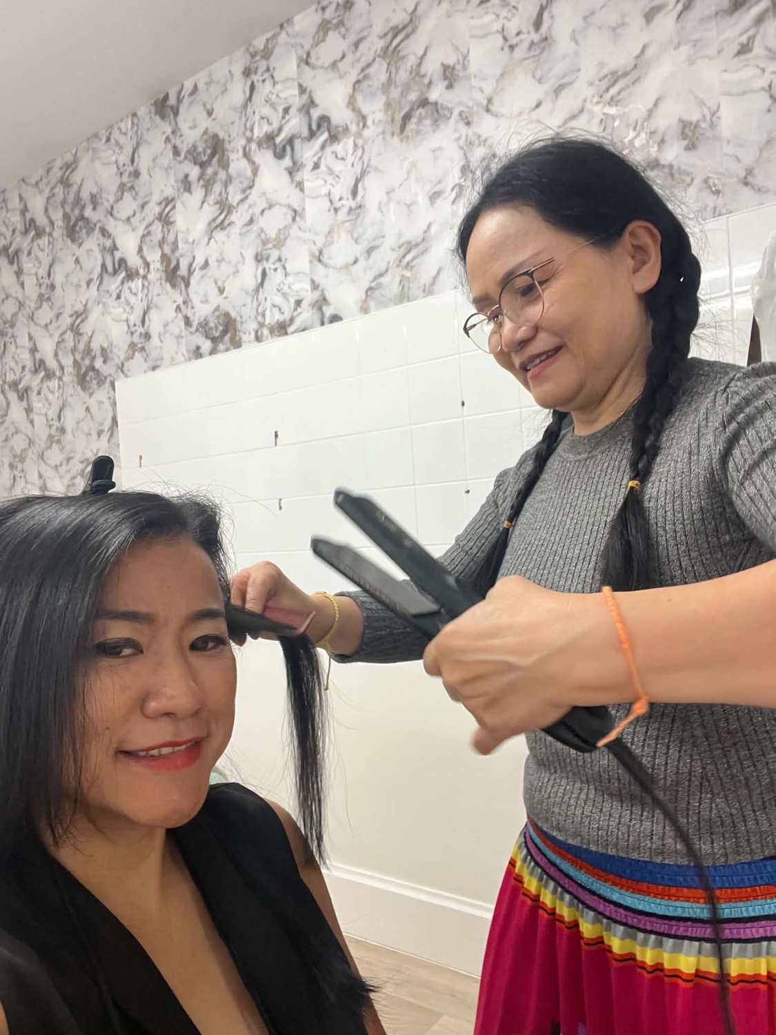 Jaruwan straightening a client's hair in the salon, both smiling